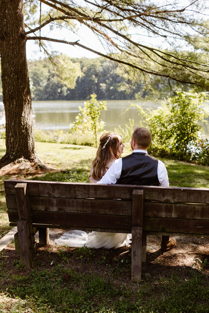 the bride and groom sitting on a bench overlooking a lake at Seneca Creek State Park in Maryland. 