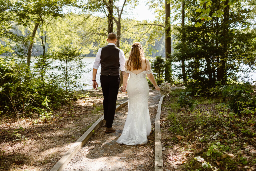 the bride and groom walking through the woods together along a lake at Seneca Creek State Park during their Maryland elopement. 