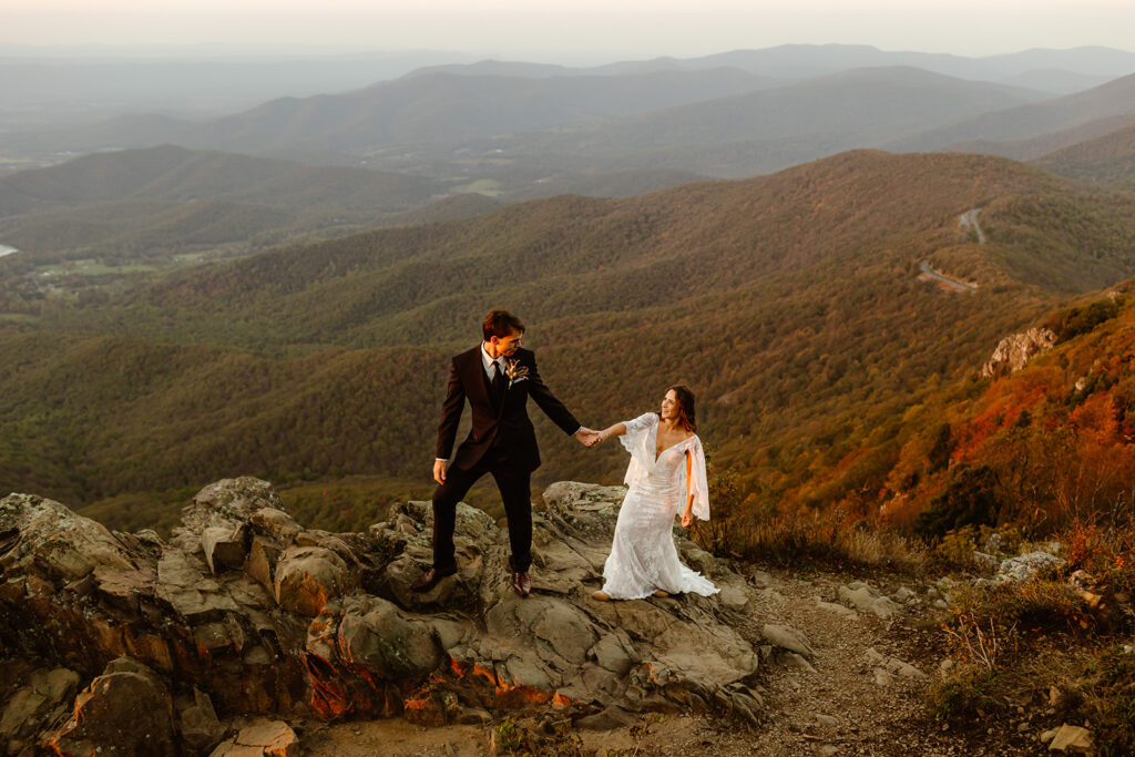 the wedding couple holding hands and walking along the Virginia mountain during their adventure elopement