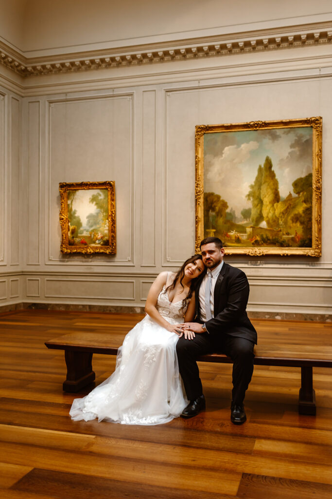 the wedding couple sitting on the bench in the art museum 