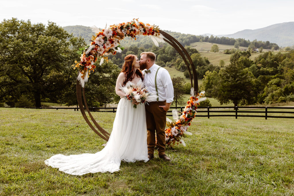 the wedding couple kissing underneath their circle wedding arbor with fall flowers