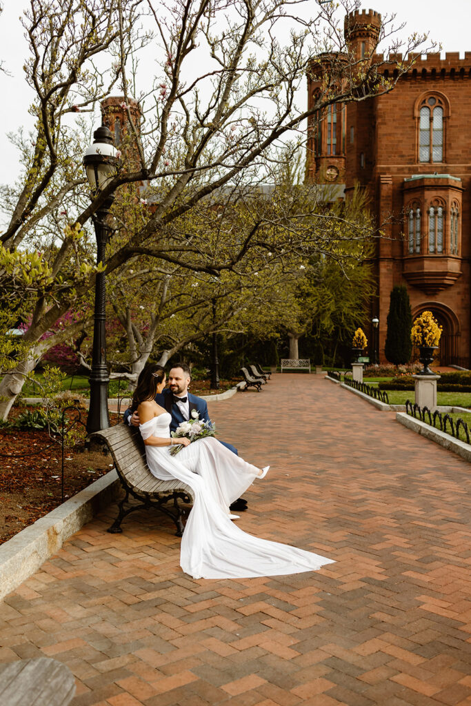 the wedding couple sitting on a bench in the gardens at the Smithsonian Castle