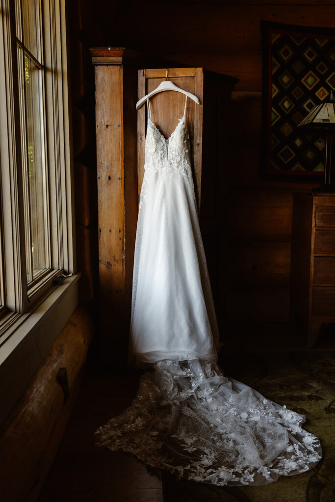 wedding dress with lace train hanging near the window