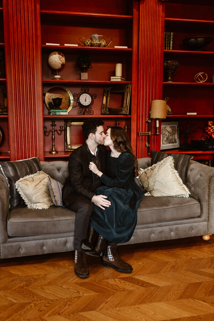 the engaged couple kissing on the couch in the red room after their surprise proposal