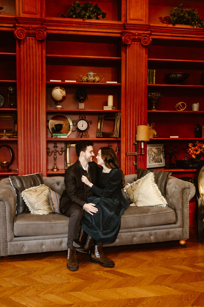 the engaged couple sitting on a red couch at the Great Marsh Estate