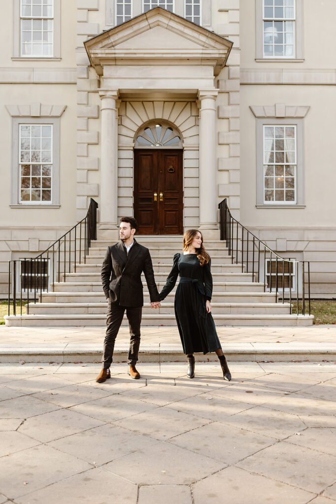 the engaged couple posing in front of the Great Marsh Estate as they look away from each other