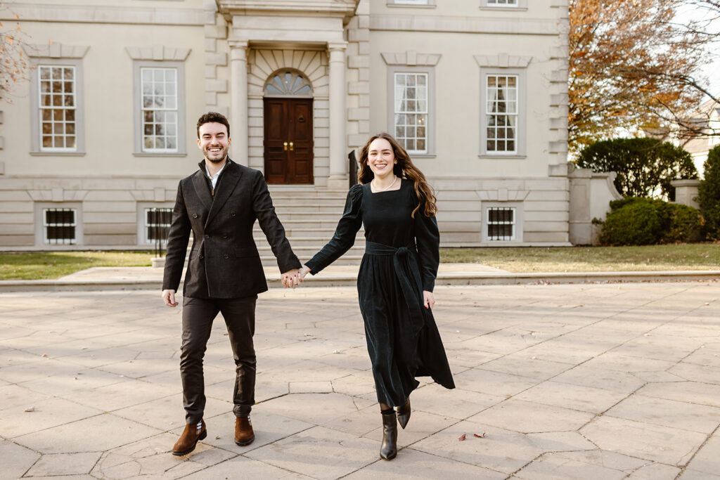 the engaged couple holding hands as they walk along the driveway of the Great Marsh Estate in Virginia