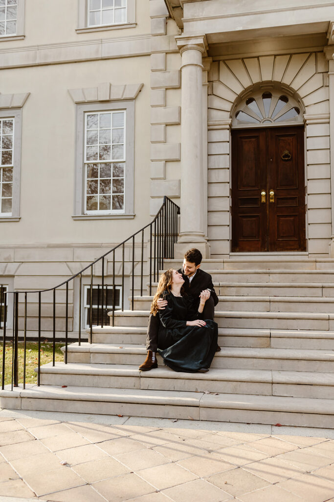 the engaged couple sitting on the steps of the Great Marsh Estate for proposal photos