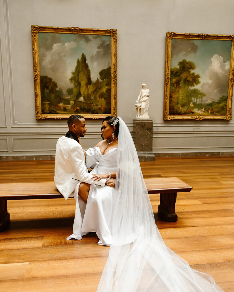 the wedding couple sitting on a bench for wedding photos