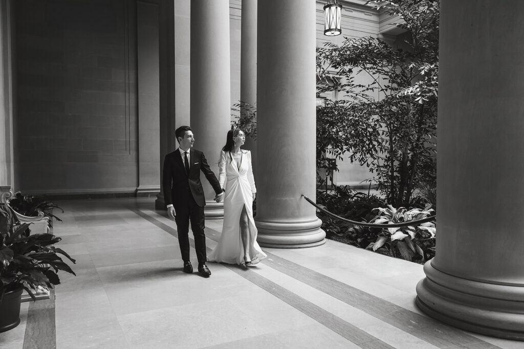 the wedding couple walking through the National Gallery of Art in a black and white wedding photo