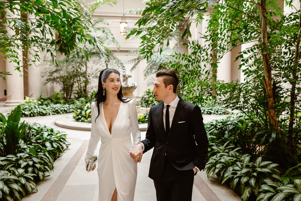 the wedding couple walking through the greenery at the National Gallery of Art