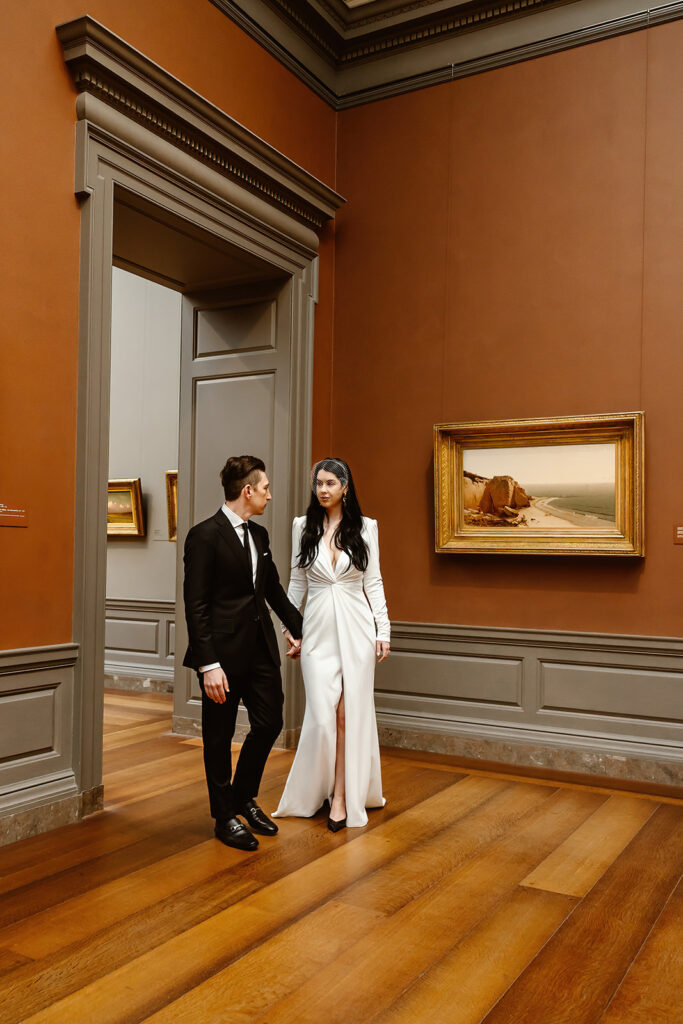 the wedding couple holding hands and walking through the National Gallery of Art