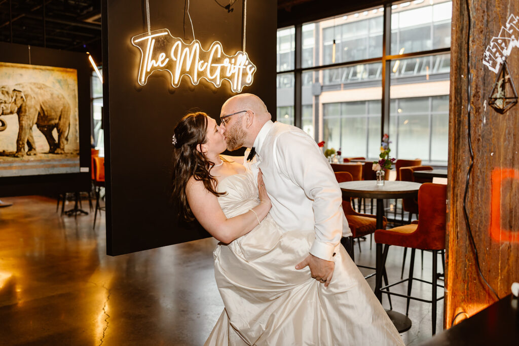 the wedding couple kissing by the banner at their wedding reception