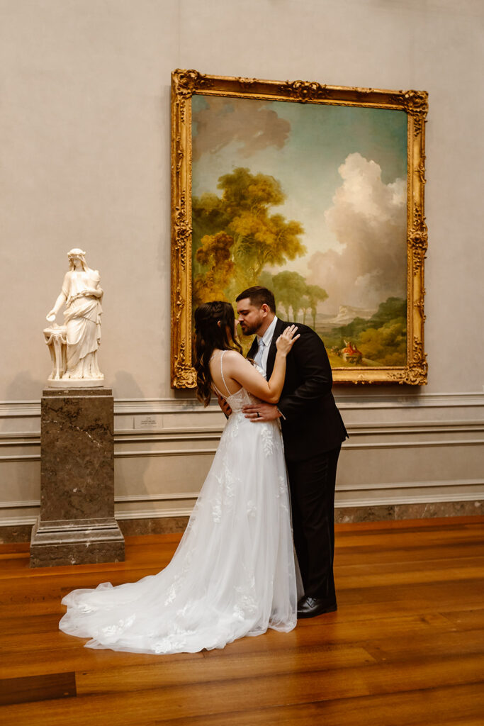 the wedding couple kissing by a painting at the art museum