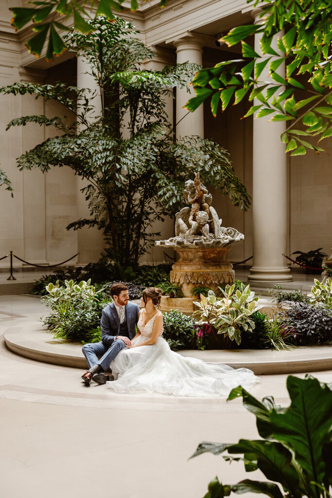 the wedding couple sitting on the ground in the National Gallery of Art by the greenery