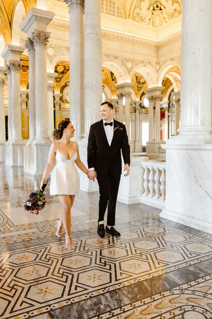 the wedding couple holding hands and walking together through the Library of Congress