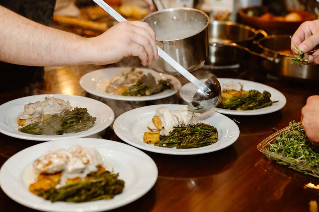 Close up photo of the private chef pouring gravy on the dinner plates about the to be served in the elopement reception. 