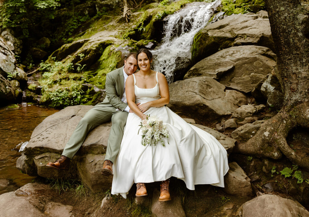 bride and groom sitting down on the rocks with a waterfall in the background