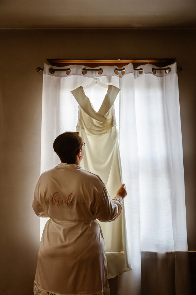 bride looking at her wedding dress hanging from the window