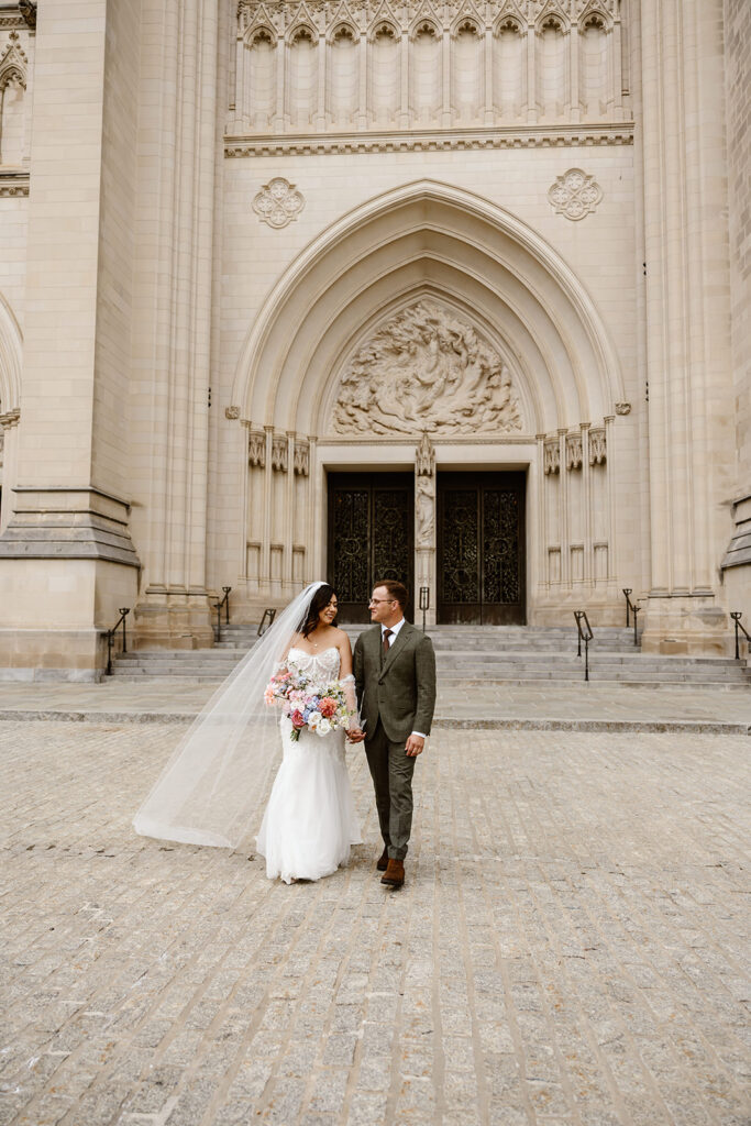 the wedding couple walking together outside of the national cathedral in Washington DC