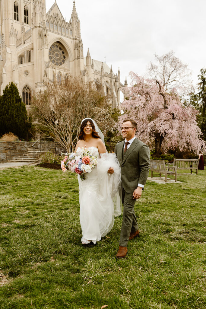 the wedding couple walking together outside of the cathedral in Washington DC with cherry blossoms in the backdrop