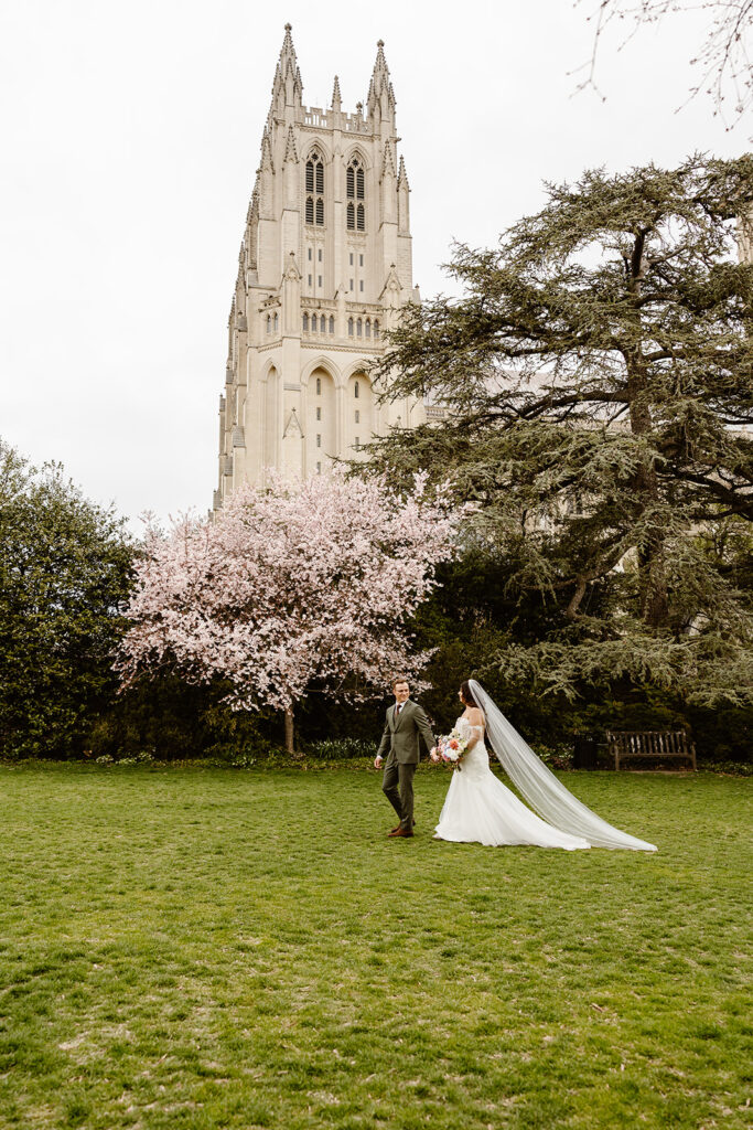 the wedding couple walking together outside of the cathedral in Washington DC with cherry blossoms in the backdrop