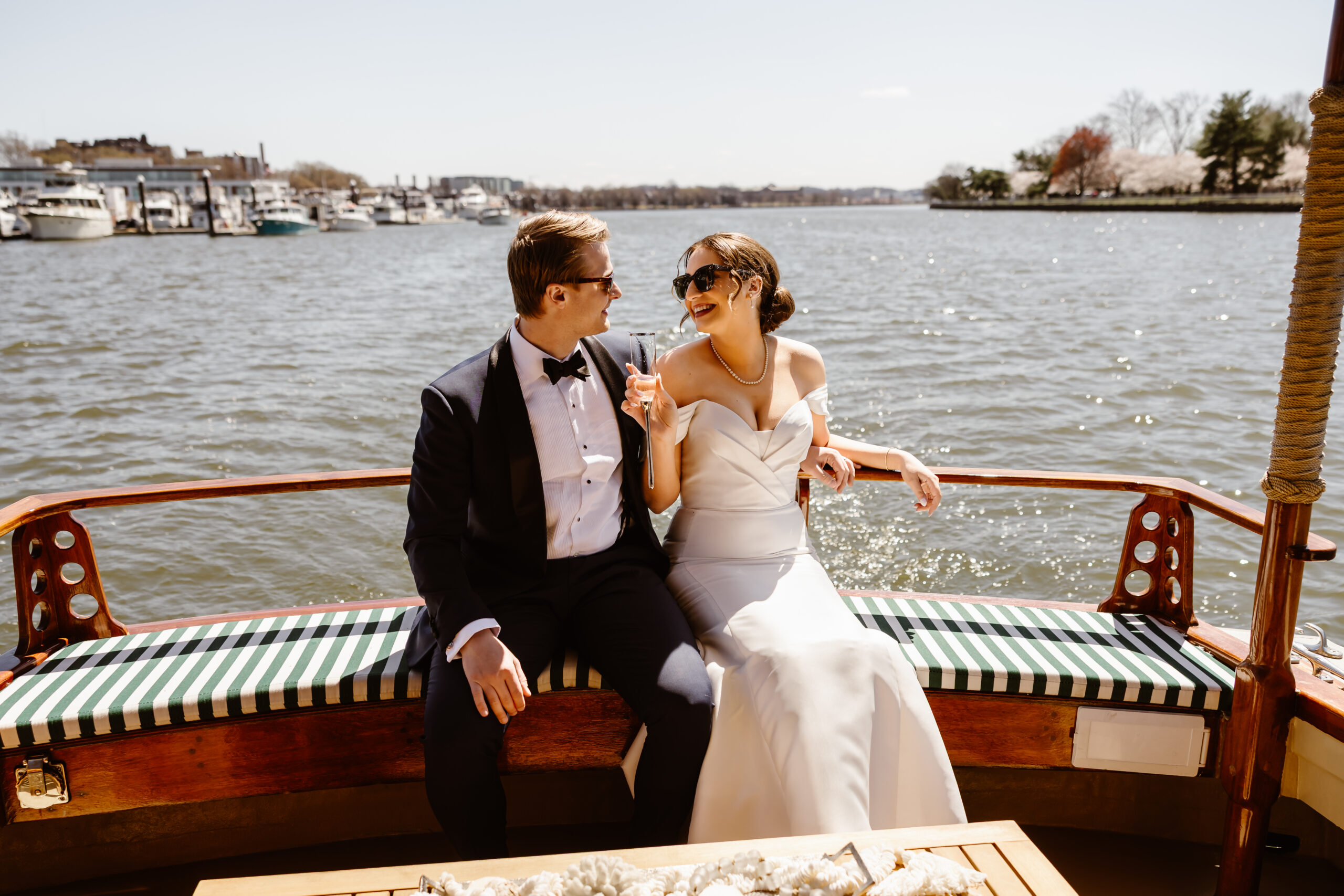 Bride and groom sit on the back of a private yacht on the Potomac River drinking champagne during their spring Washington DC elopement.