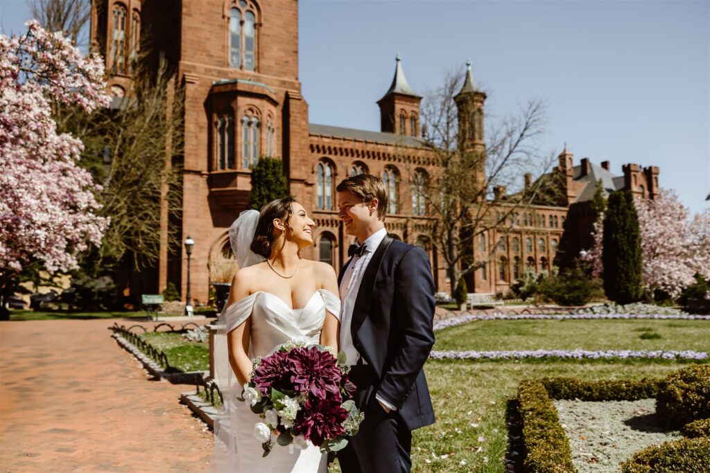 bride and groom with pink blossoms in the background at the smithsonian castle garden