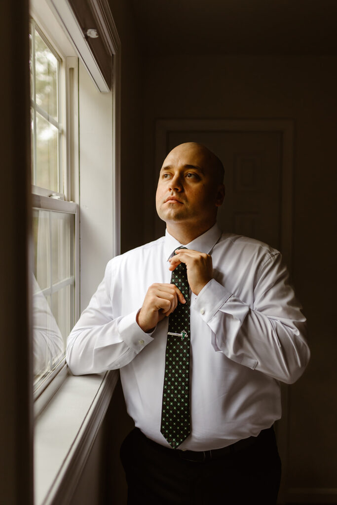 groom getting ready next to a window at the airbnb