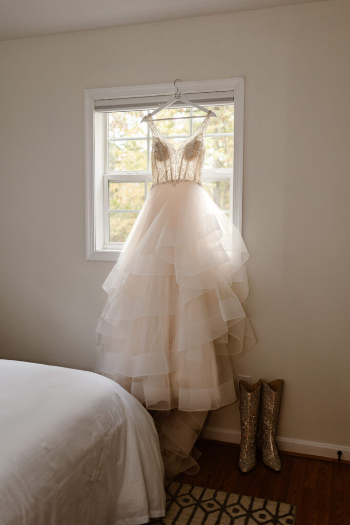 beautiful elopement dress hanging from the window with sparkly boots next to it