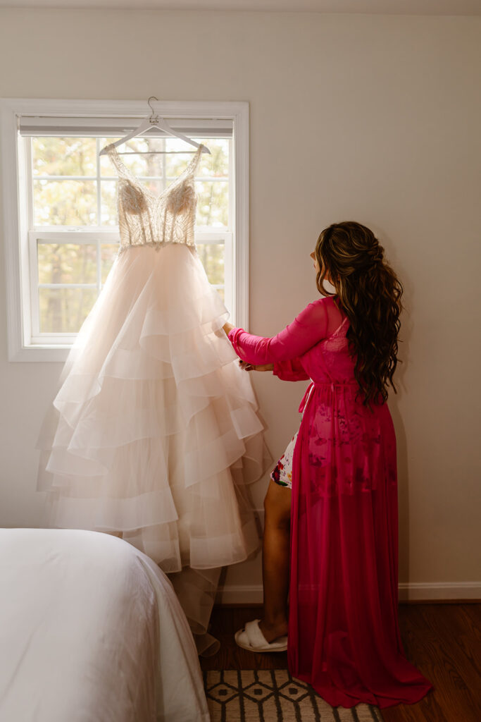 bride looking at her beautiful elopement dress hanging off the window
