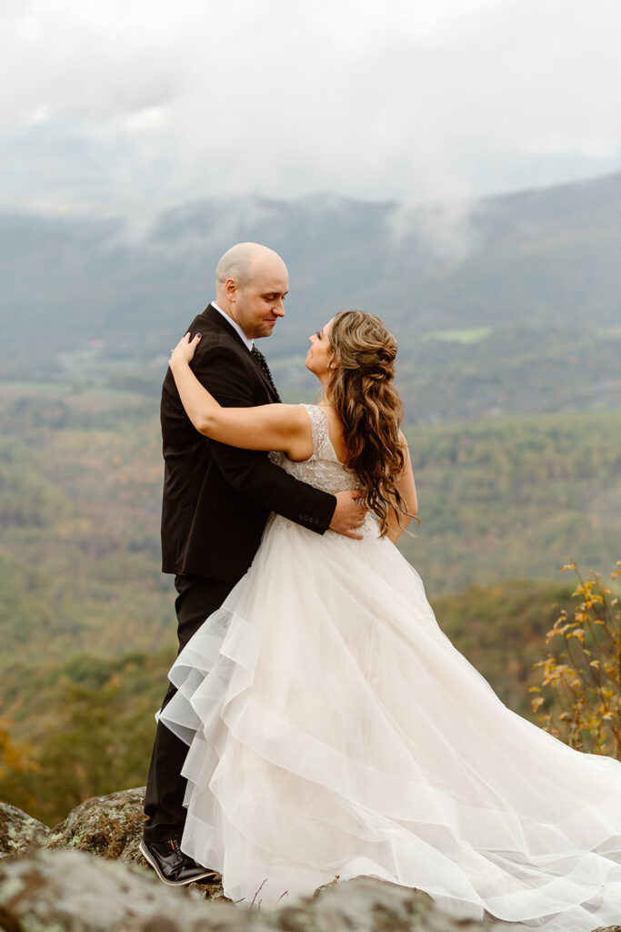 bride and groom hugging on foggy overlook at Stony Man summit in Shenandoah during their Shenandoah National Park elopement in October with fall foliage in the backdrop