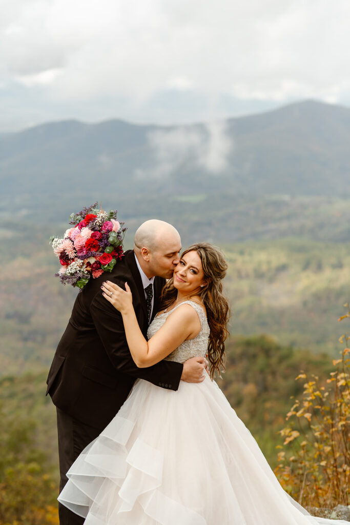 bride and groom hugging on foggy overlook at Stony Man summit in Shenandoah during their Shenandoah National Park elopement in October with fall foliage in the backdrop