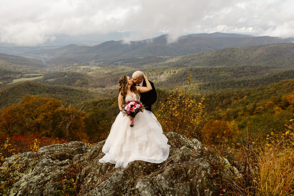 bride and groom hugging on foggy overlook at Stony Man summit in Shenandoah during their Shenandoah National Park elopement in October with fall foliage in the backdrop