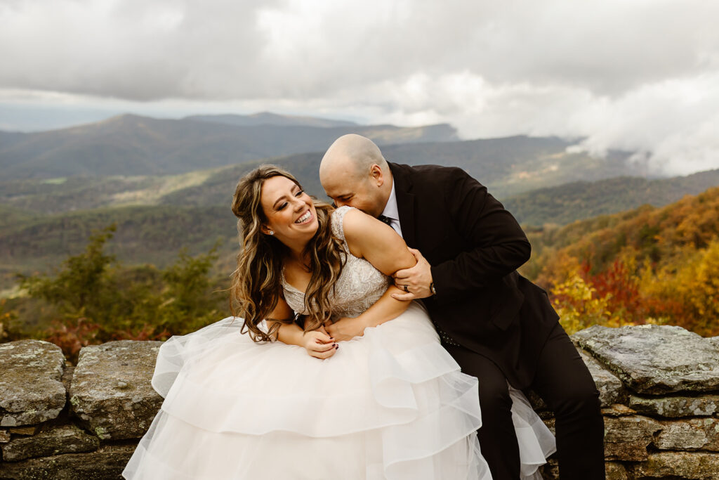bride and groom sitting in front of a foggy overlook at Stony Man summit in Shenandoah during their Shenandoah National Park elopement in October with fall foliage in the backdrop