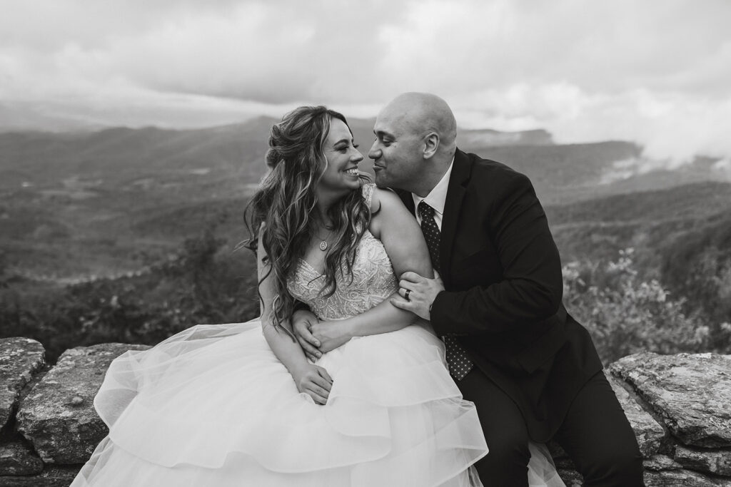 bride and groom sitting in front of a foggy overlook at Stony Man summit in Shenandoah during their Shenandoah National Park elopement in October with fall foliage in the backdrop