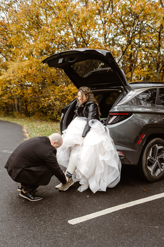 groom helping his bride change shoes at the back of the car