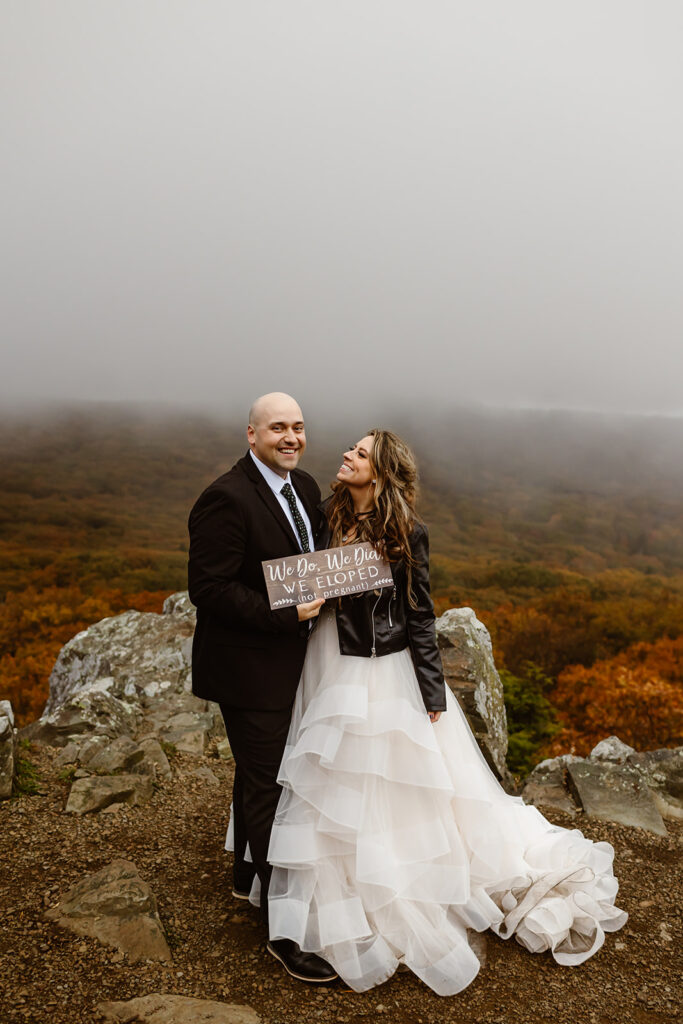 bride and groom holding their custom just eloped sign surrounded by fall foliage during their shenandoah elopement