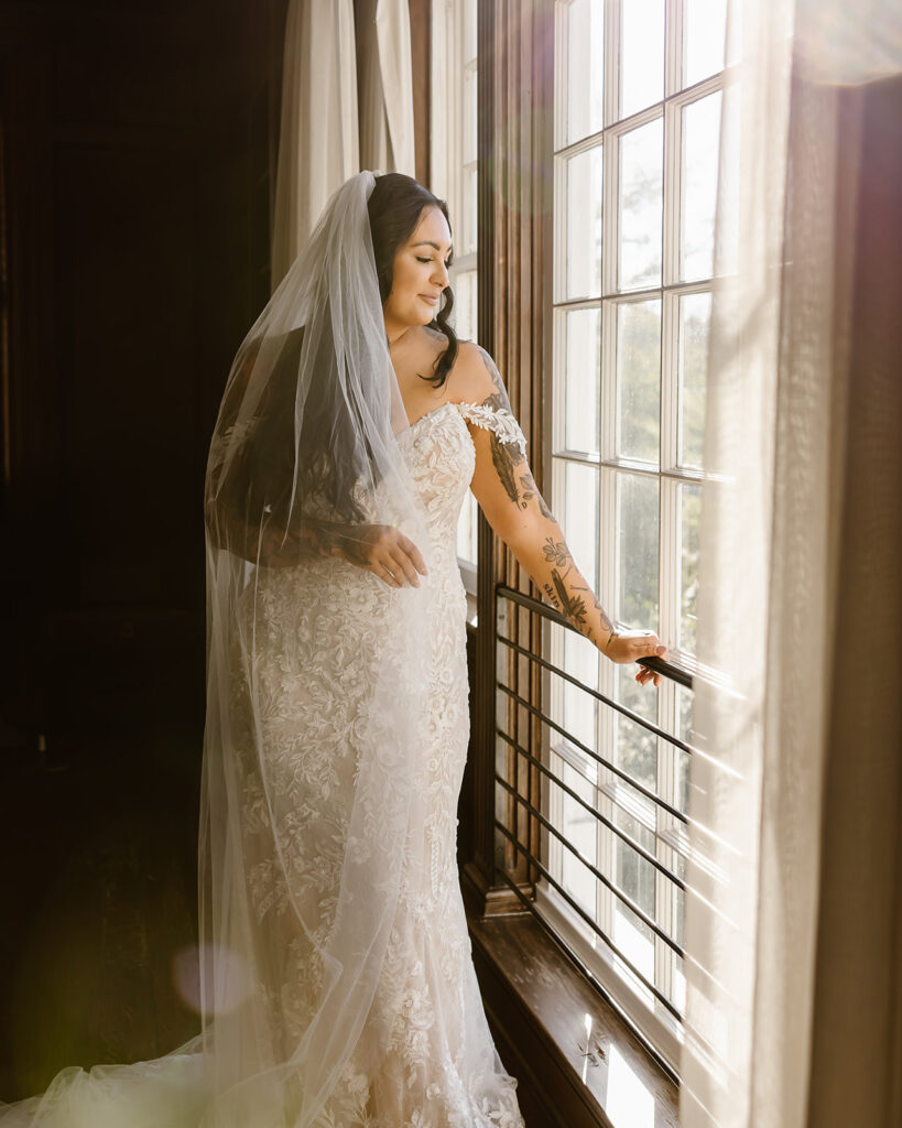 stunning bride in her lace gown posing by a window