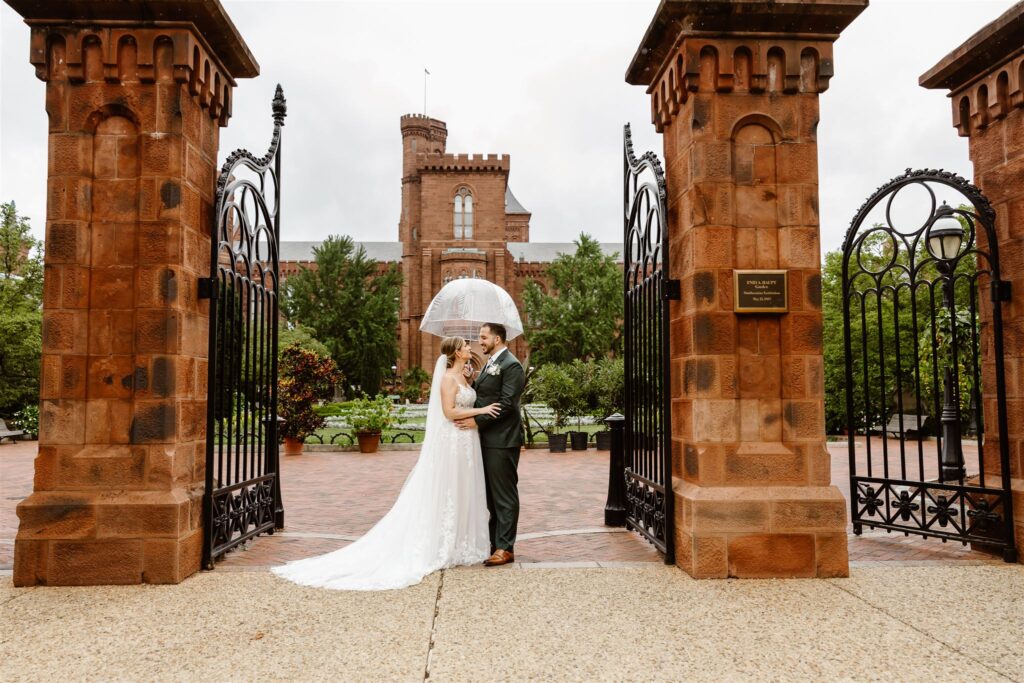 sweet bride and groom under clear umbrellas during rainy moments at the smithsonian castle garden