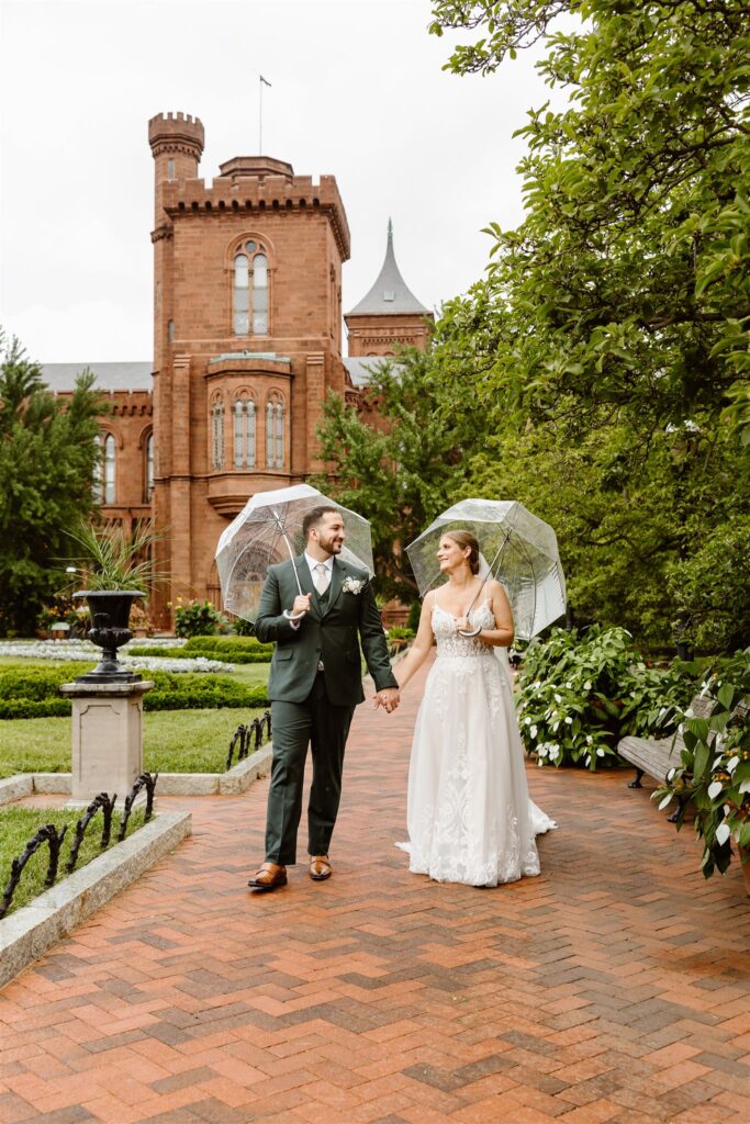 sweet bride and groom under clear umbrellas during rainy moments at the smithsonian castle garden