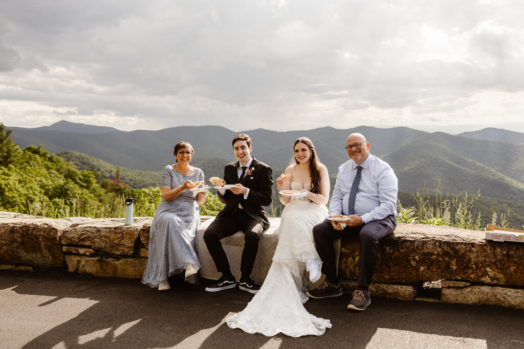 bride and groom and parents sharing pizza in shenandoah national park for a post elopement reception celebration