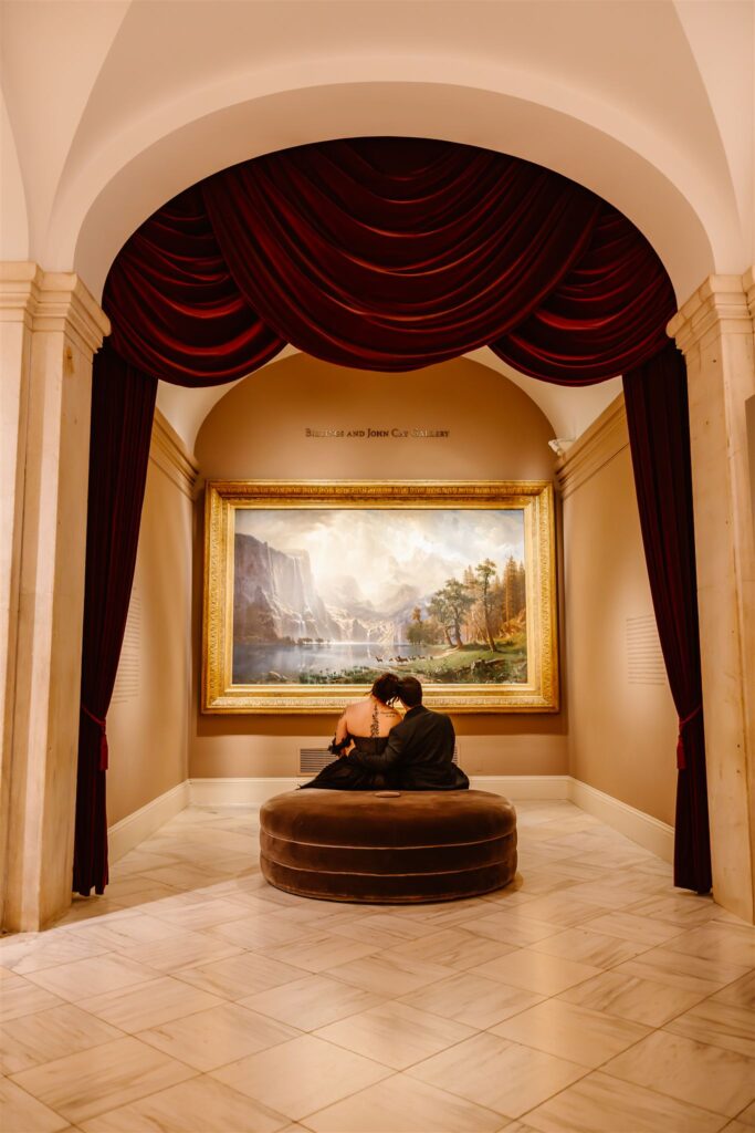 bride and groom sitting in front of a painting at the national portrait gallery 