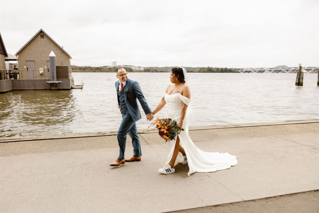bride and groom walking hand in hand next to a waterfront in Northern virginia