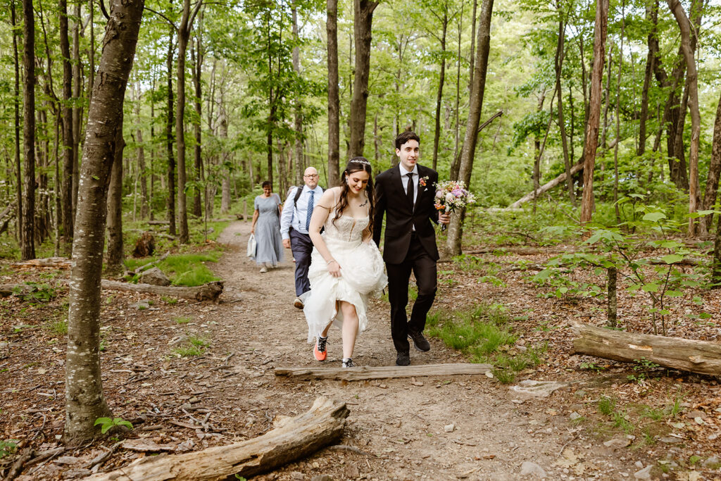bride and groom holding hands as they are hiking through a forest with their guests during their shenandoah national park elopement