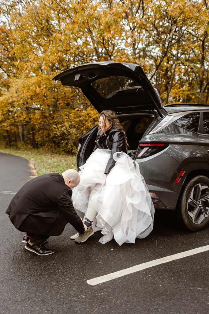 groom helping bride put on hiking shoes at the back of the car