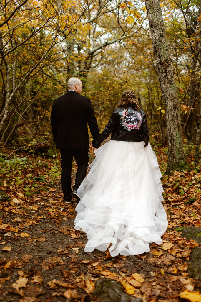 bride and groom holding hands as they are hiking through a forest covered in fall colors during their shenandoah national park elopement