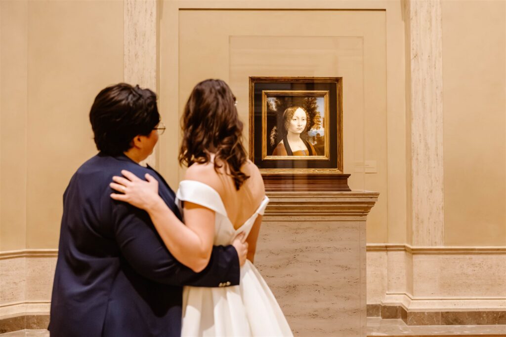 the wedding couple hugging by a painting at the art museum