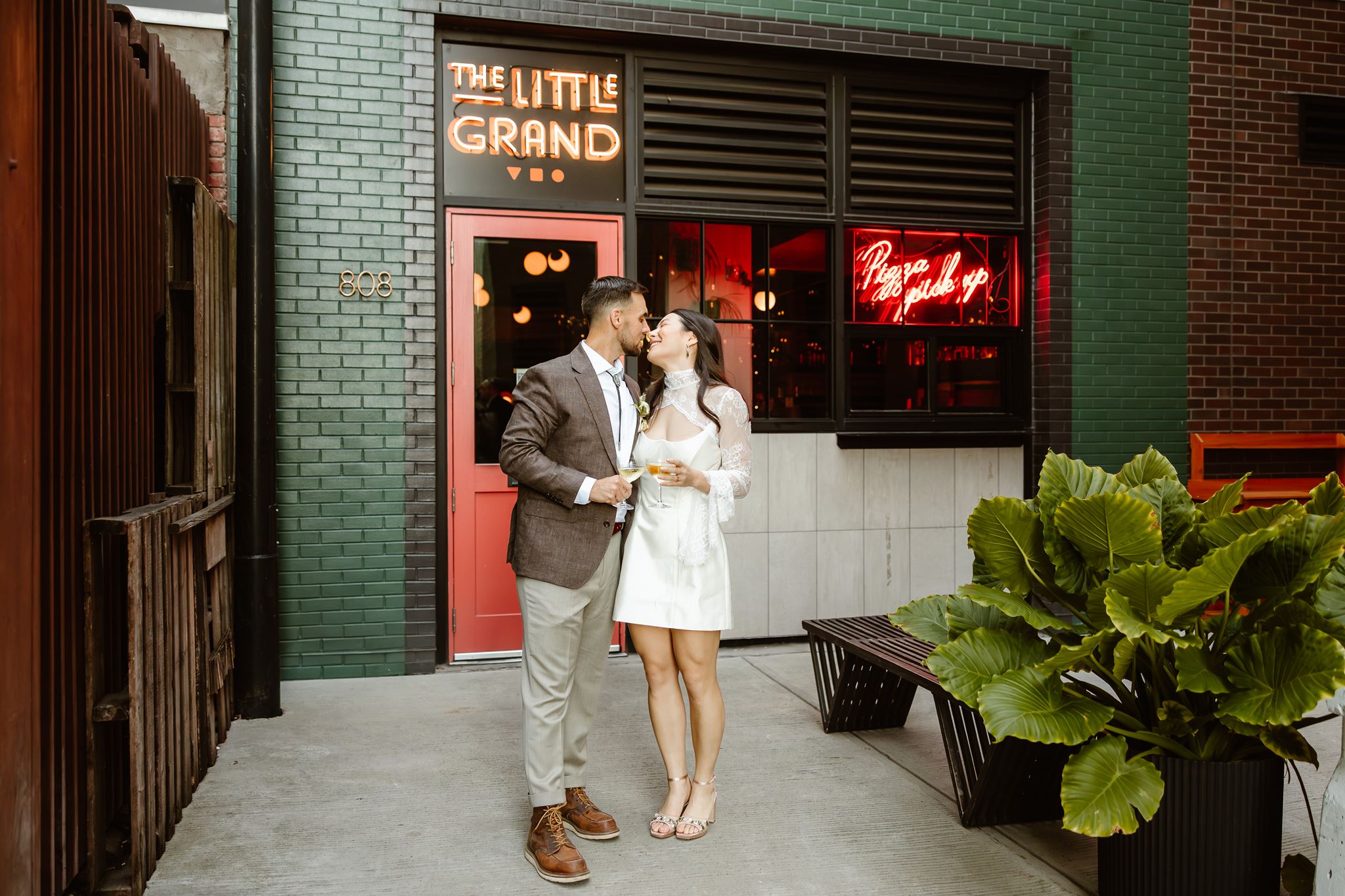 wedding couple posing in front of the door of the little grand pizza shop
